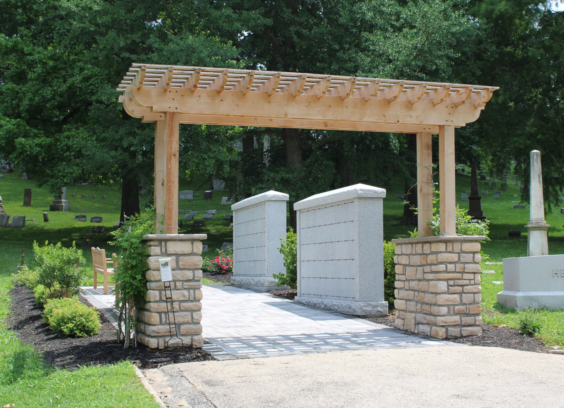 Granite columbarium niche walls in a cemetery memorial garden with a cedar pergola