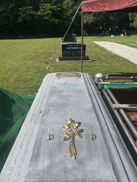 Sealed burial vault with bronze rose emblem and nameplate at a graveside service